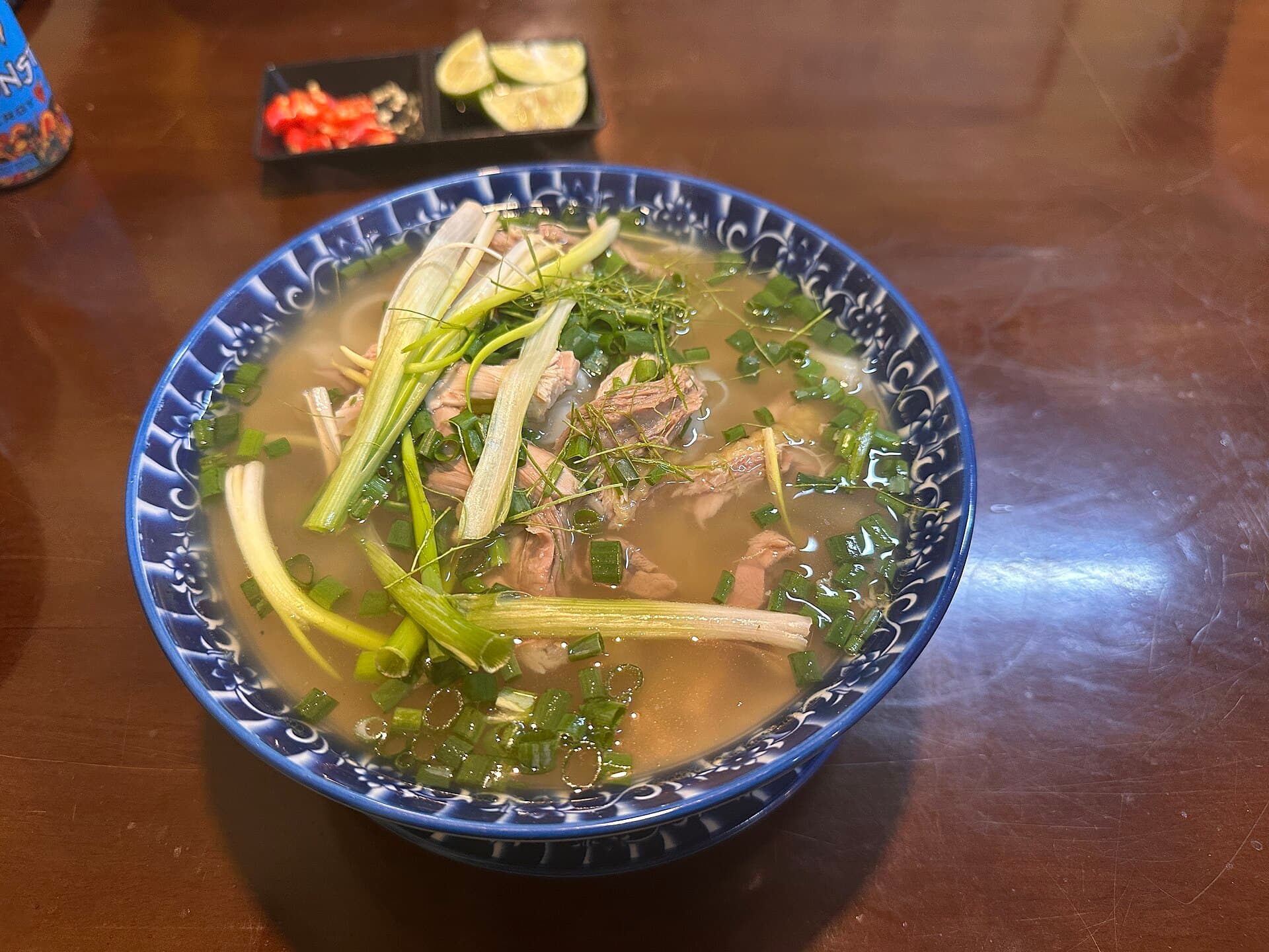 A bowl of Vietnamese pho with herbs, scallions, lime, and chili on a wooden table — the $2 street meal that anchors every Vietnam travel budget